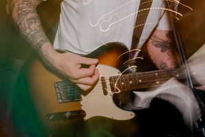 Tattooed musician plays electric guitar with blurred motion during dynamic live performance.