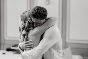 A tender black and white moment captured as two people share an intimate embrace in an elegant room.