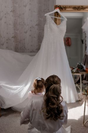 A beautiful white wedding dress hangs on display while two people with elegant hairstyles admire it from below.