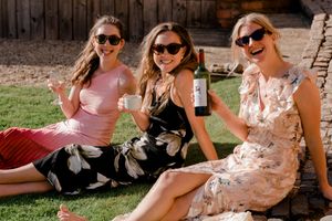 A group of people wearing sunglasses and casual summer outfits relax together in a sunny outdoor setting.
