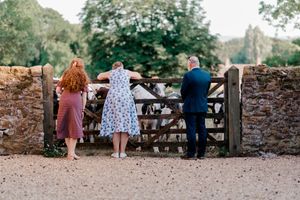 Three people stand at a rustic wooden gate overlooking a countryside view on a summer day.