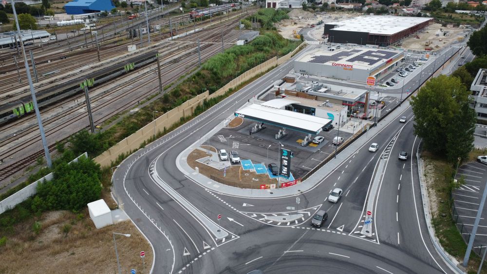 Aerial drone view of a Prio fuel station with roundabout access roads and railway tracks nearby.