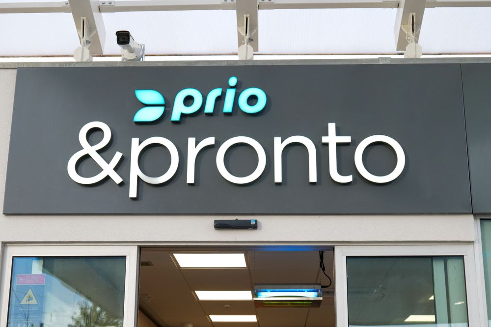 Prio and Pronto convenience store exterior signage with turquoise logo on dark grey facade above entrance.