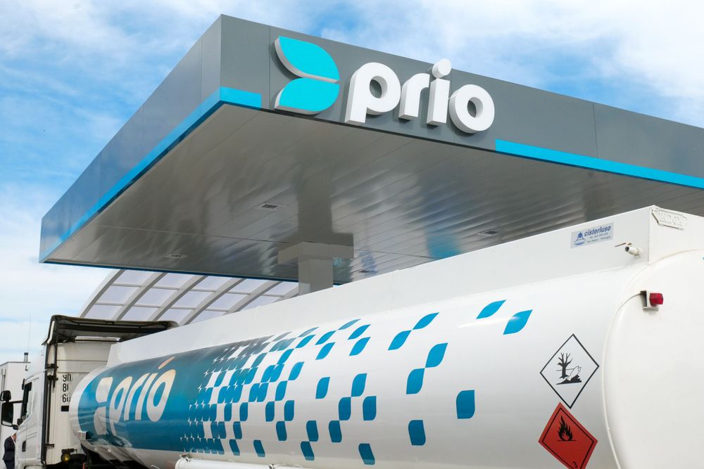 Prio branded fuel tanker truck parked under a modern gas station canopy on a sunny day.