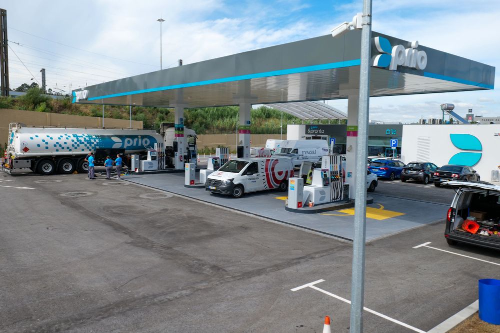 Prio fuel station forecourt with branded tanker truck, multiple pump lanes, and vehicles refueling.