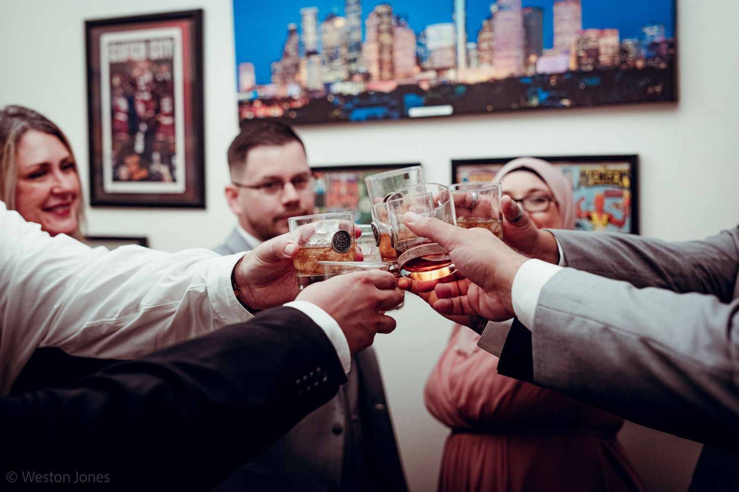 Group of people toasting glasses in celebration with city skyline artwork on wall.