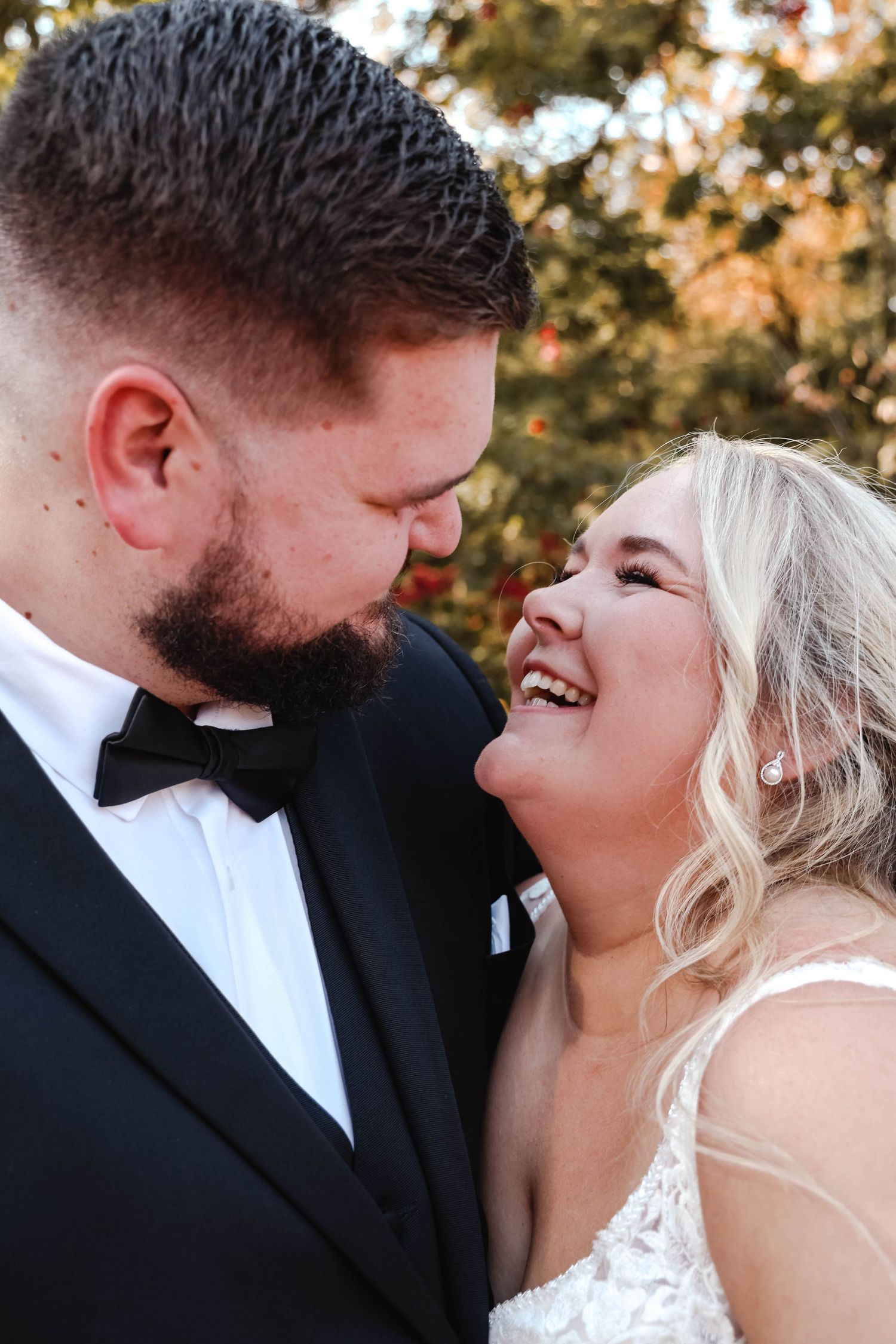 A joyful bride in white and groom in black bow tie share an intimate laughing moment during their wedding day.