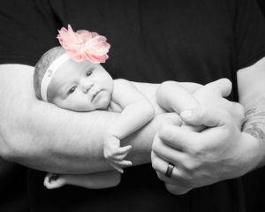 Black and white portrait of newborn baby with pink flower headband cradled in hands.