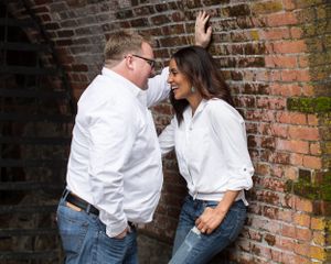 A romantic couple in white shirts sharing an intimate moment against a brick wall.