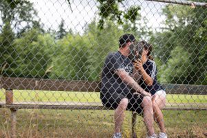 Two people sitting together behind a chain link fence in a park setting.