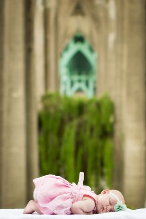 Baby in pink dress lying beneath St. Johns Bridge in Portland with blurred gothic architecture.