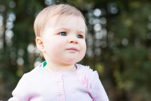 Baby in pink sweater looks up with wonder against blurred forest background.