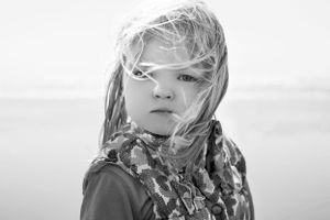 Artistic black and white portrait of child with windswept hair wearing scarf.