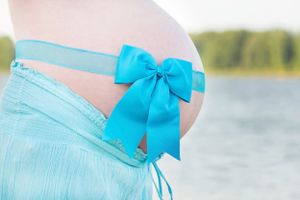 A pregnant belly adorned with a turquoise bow against a waterfront backdrop.