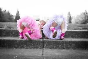 Two figures in pink and purple tutus bending down on concrete steps in selective color photo.