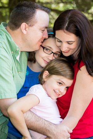 A loving family cuddles together closely outdoors in casual clothing on a sunny day.