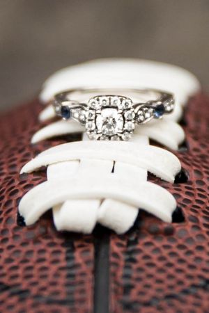Diamond engagement ring nestled in white football laces against brown leather background.
