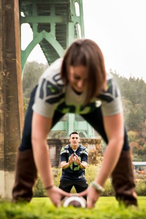 Creative football-themed engagement photo with couple posing under St Johns Bridge in Portland.
