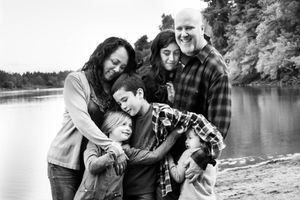 A black and white family portrait captured outdoors by a lake.