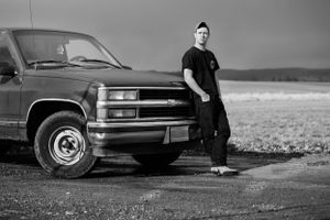 A person in black clothing standing beside a large pickup truck in a rural field.