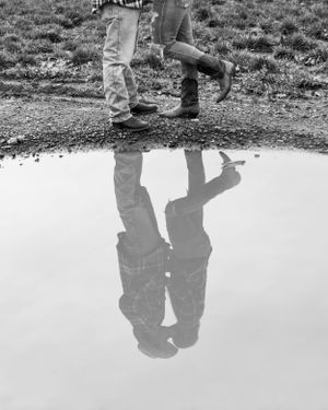 Reflection of two people standing by a puddle in black and white photography.