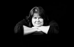 A dramatic black and white portrait with someone resting their chin on folded arms.