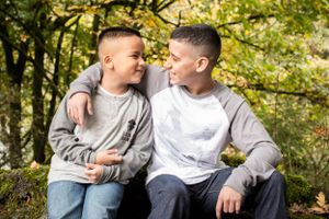 Two boys in grey sweaters sharing a laugh while sitting outdoors in autumn.