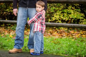 A small child in plaid and jeans stands next to an adult's legs on a path.