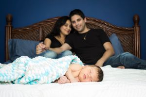 Sleeping newborn on bed with parents watching from headboard.
