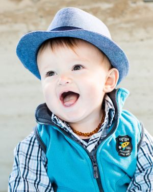 Cheerful baby wearing a blue hat and plaid shirt smiles with delight in outdoor portrait.