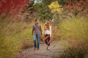 Couple walking hand-in-hand on a garden path surrounded by colorful autumn grasses and foliage.