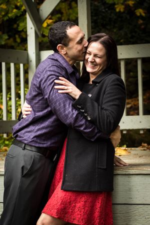Romantic couple embracing and laughing on wooden gazebo during autumn.