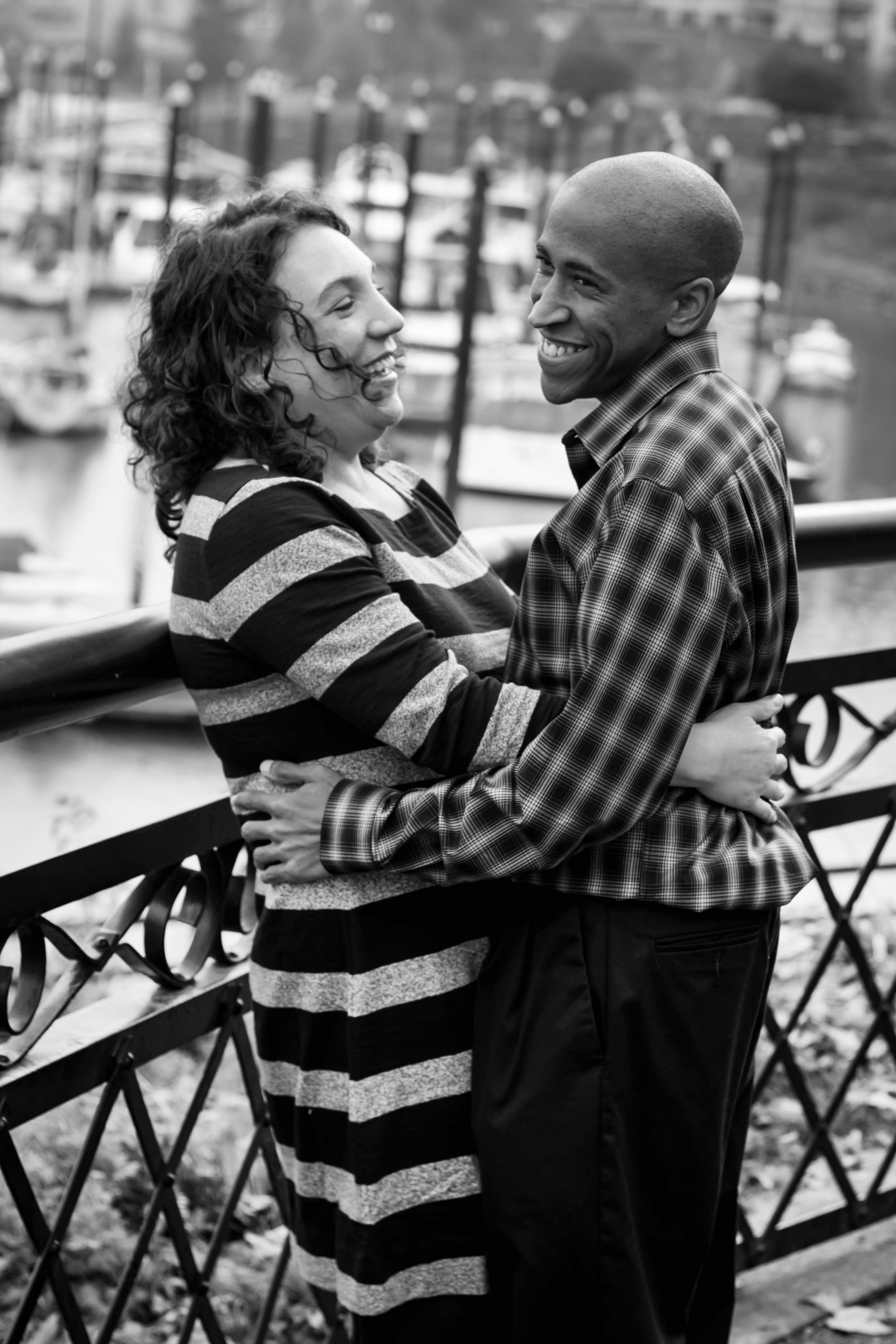 Romantic couple embrace and laugh together at sunset on a balcony overlooking a marina.