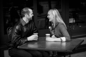 Two people engaged in conversation while having coffee at a small cafe table.