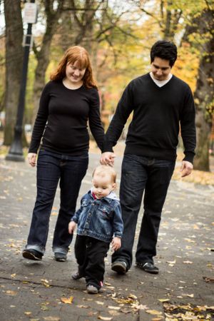 Family walking together on an autumn path holding hands with their young toddler.