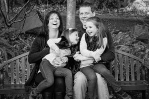 A family shares joyful laughter while sitting together on a wooden park bench.