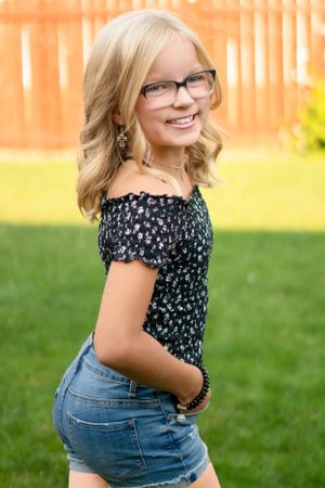 Summer portrait of young person in floral top and denim shorts smiling in backyard.