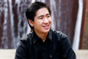 Portrait of young man in black shirt smiling against wooden wall background.