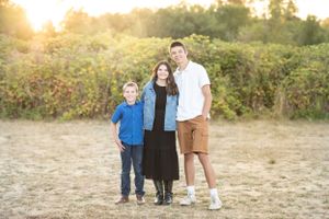 Family of three poses together at sunset in casual attire against natural backdrop.