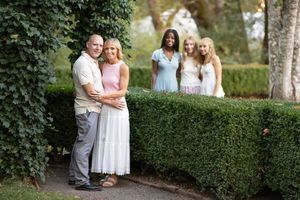 Family of four posing in a lush garden with trimmed hedges, two adults in front and two girls standing behind.