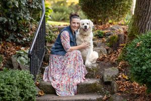 A golden retriever and companion sit together on stone garden steps surrounded by autumn leaves.