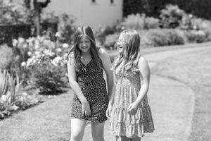 Two friends standing together in a garden wearing summer dresses in black and white photography.