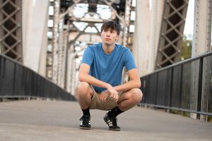 Person in blue t-shirt and shorts sits in various poses on an industrial bridge or walkway structure.