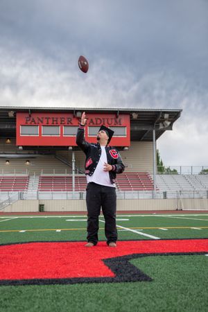 Student in letterman jacket tosses football at Panther Stadium during senior portrait session.