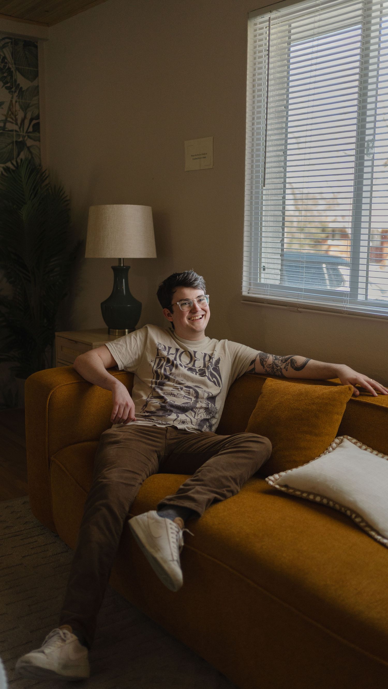 Casual portrait of person relaxing on mustard yellow couch near window.