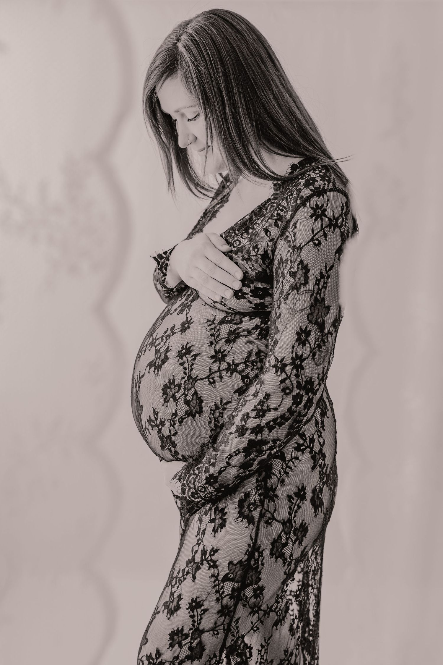 Black and white photo of a pregnant woman in a floral lace dress cradling her baby bump.