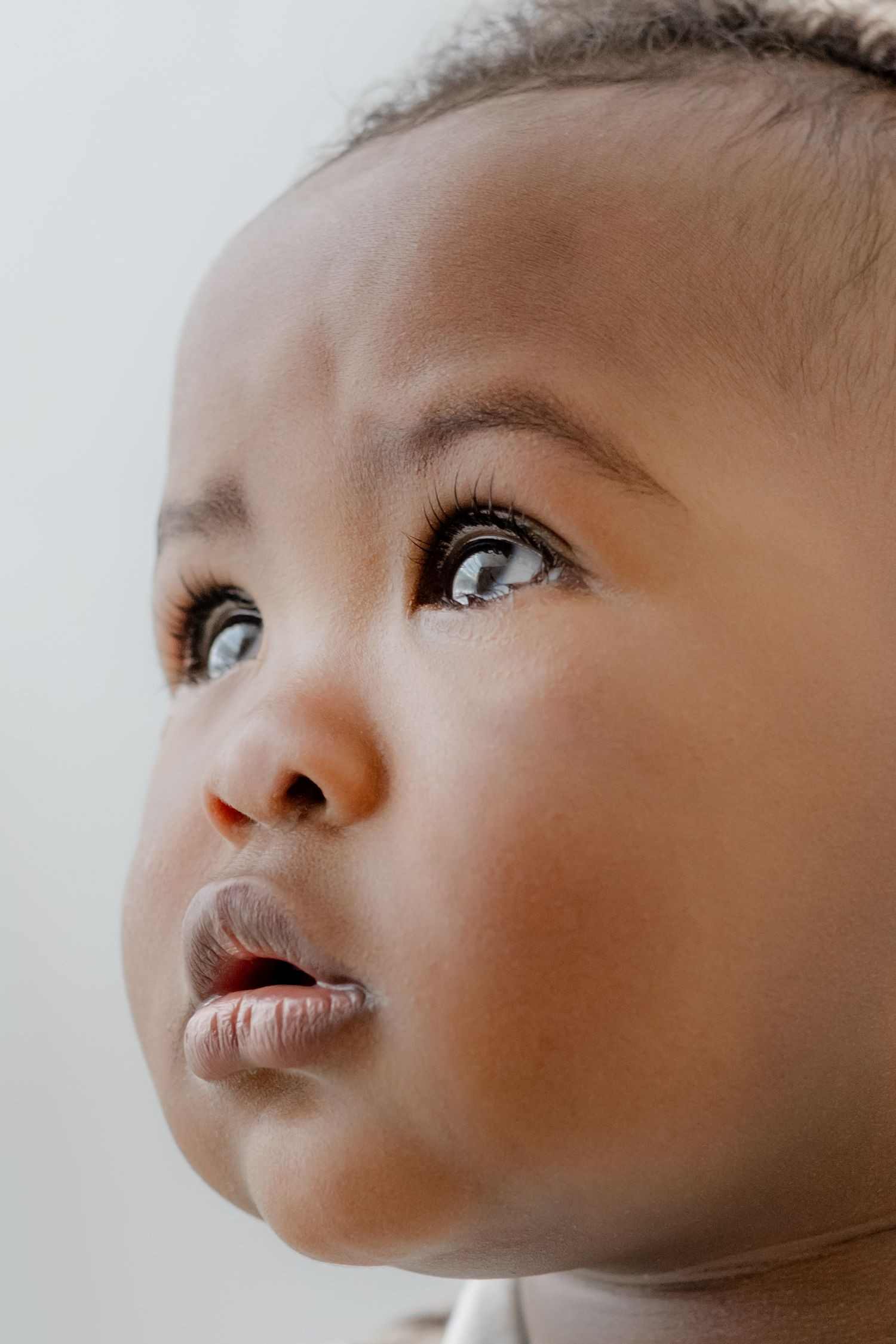 Close-up portrait of an adorable baby with bright blue eyes and dark skin looking upward with curiosity.