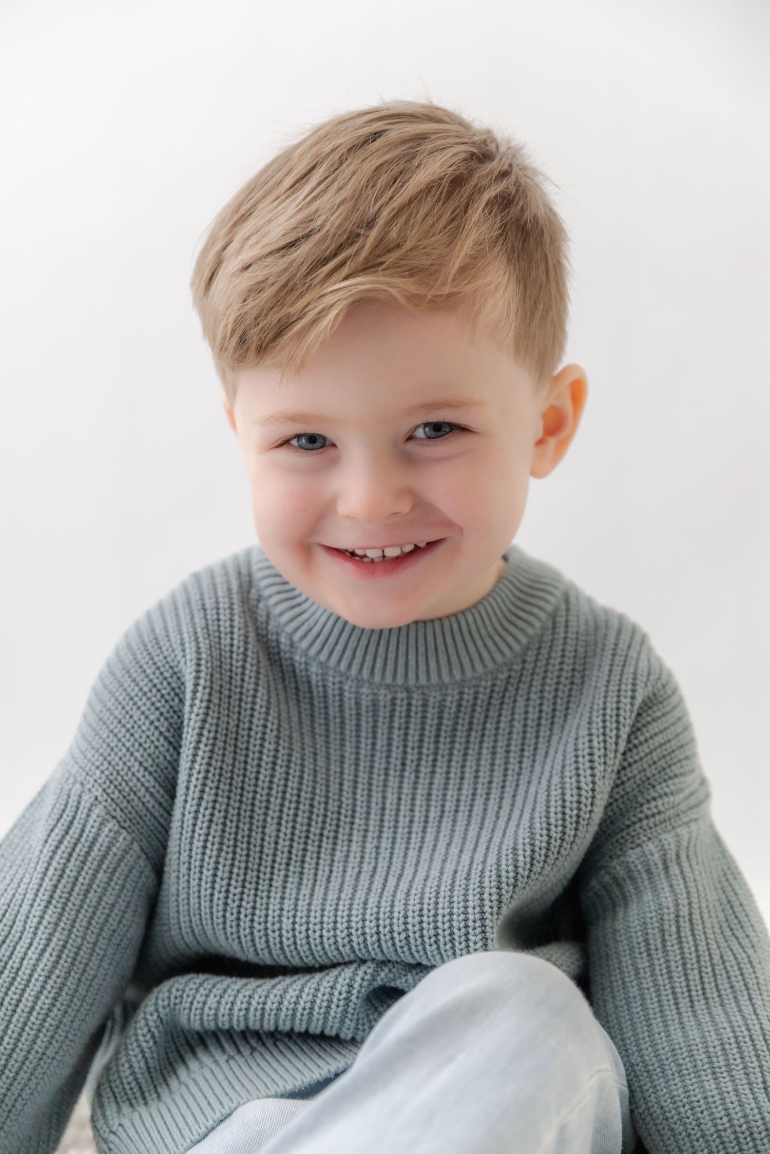 A child in a cozy sage green sweater smiles warmly against a white background in a series of candid expressions.