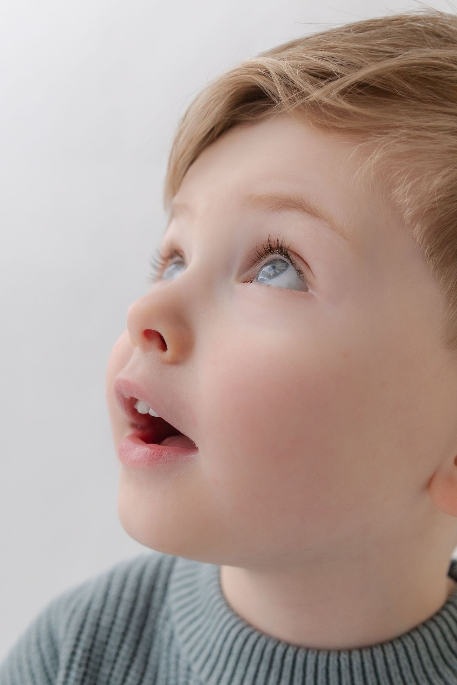 Close-up profile view of a young child with blue eyes looking upward while wearing a gray sweater.