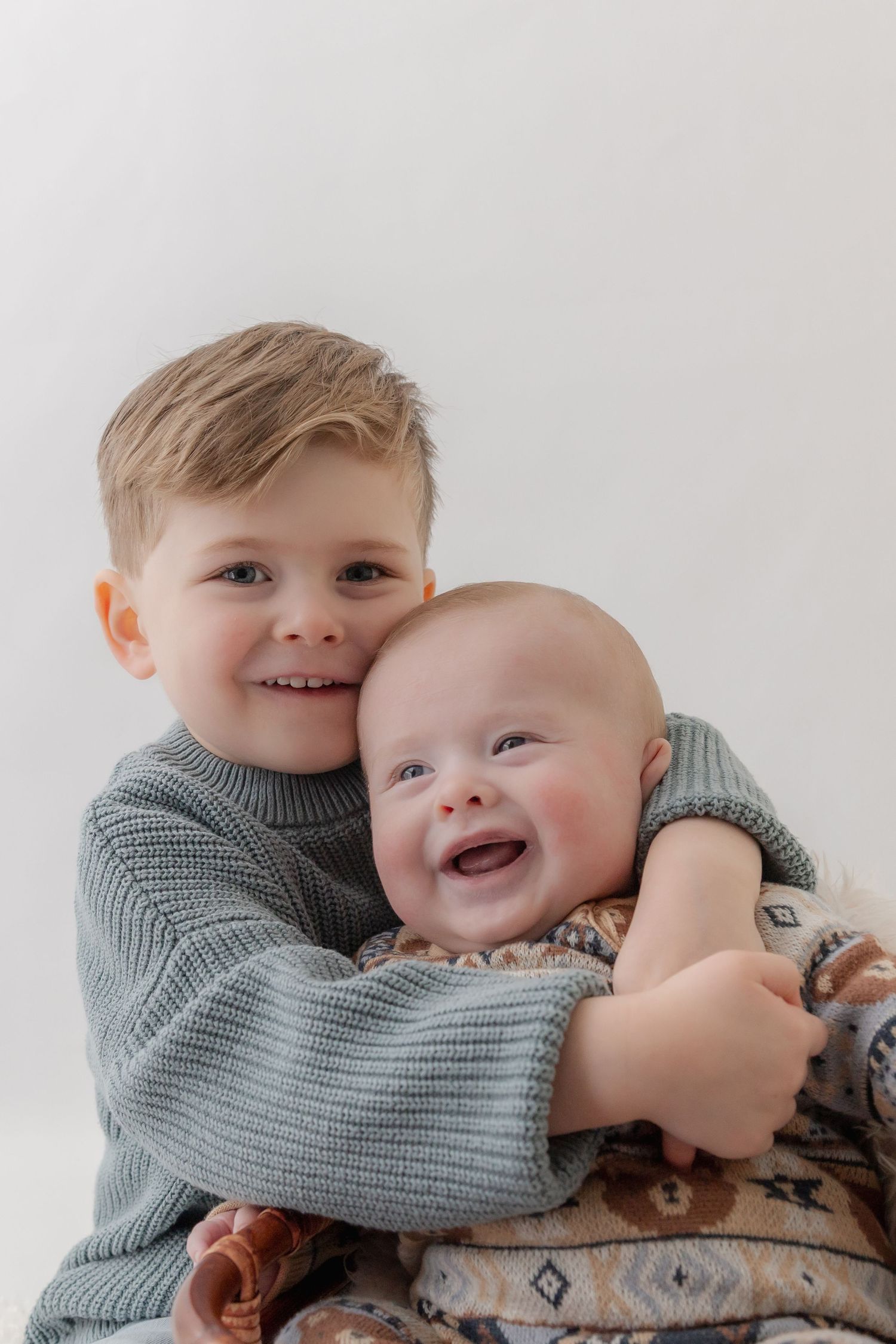 Two children in matching gray sweaters share a joyful embrace while laughing together.